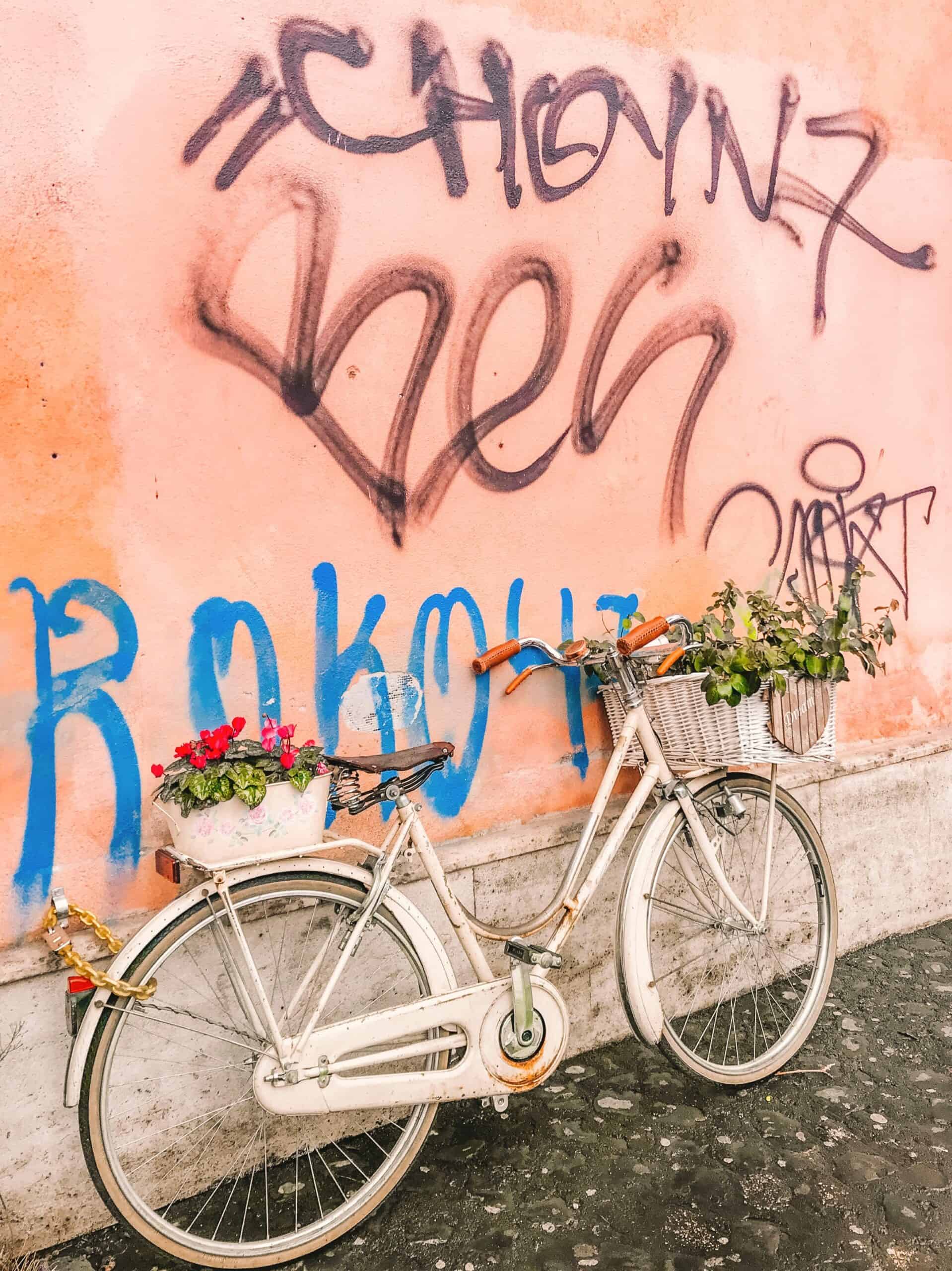 A bike covered in flowers propped against a graffiti-covered wall in Trastevere. 
