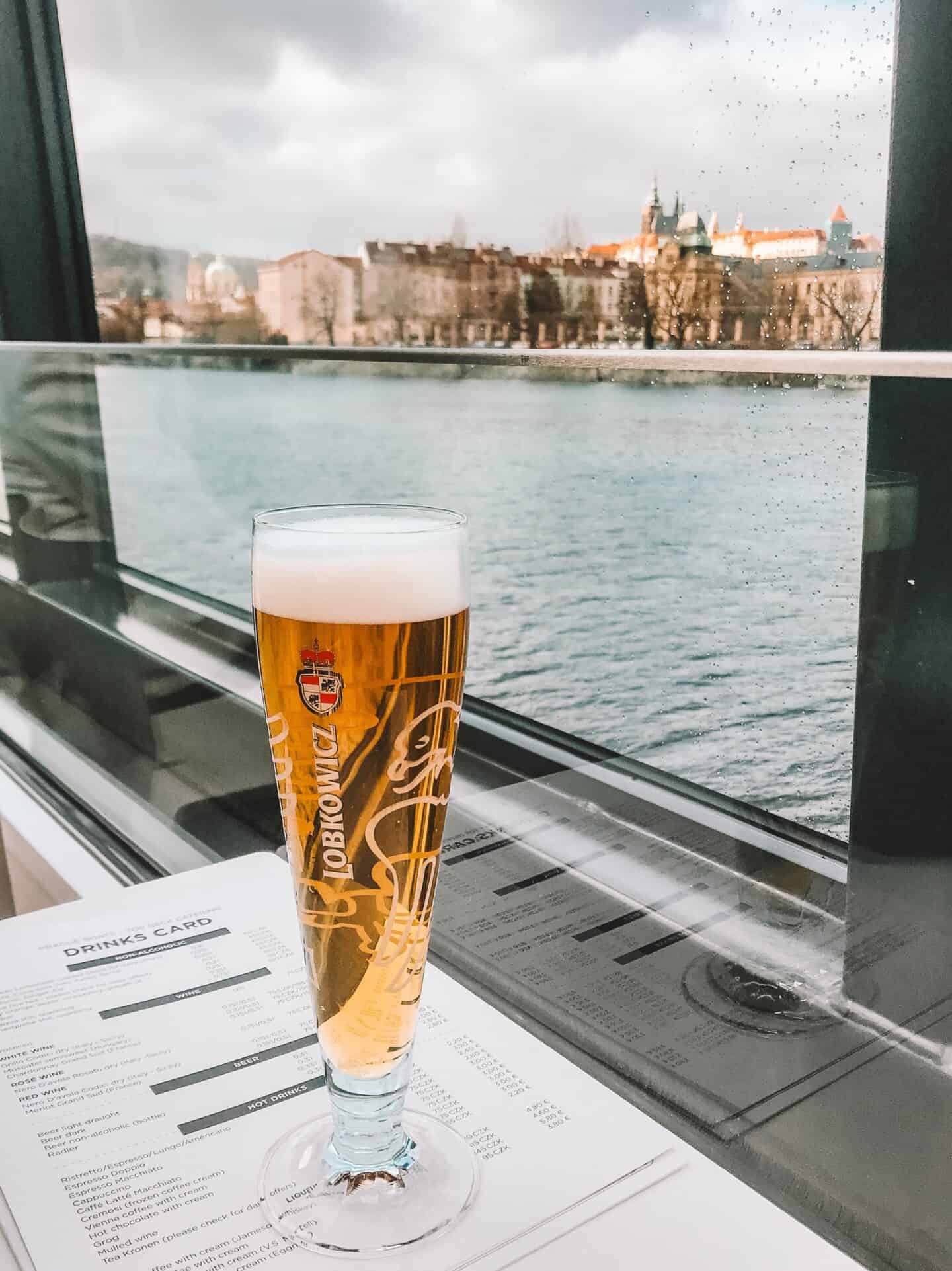 Enjoying a Czech beer with a view of Prague on a Vltava River cruise.
