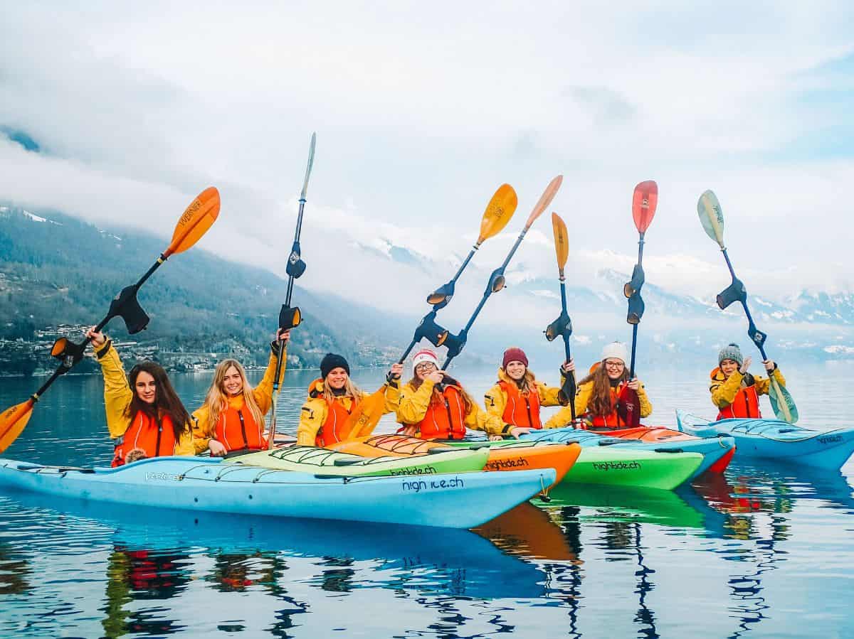 Me and my new friends on a winter kayaking excursion in Interlaken. There's 7 of us in brightly colored kayaks holding up our paddles on Lake Brienz. 