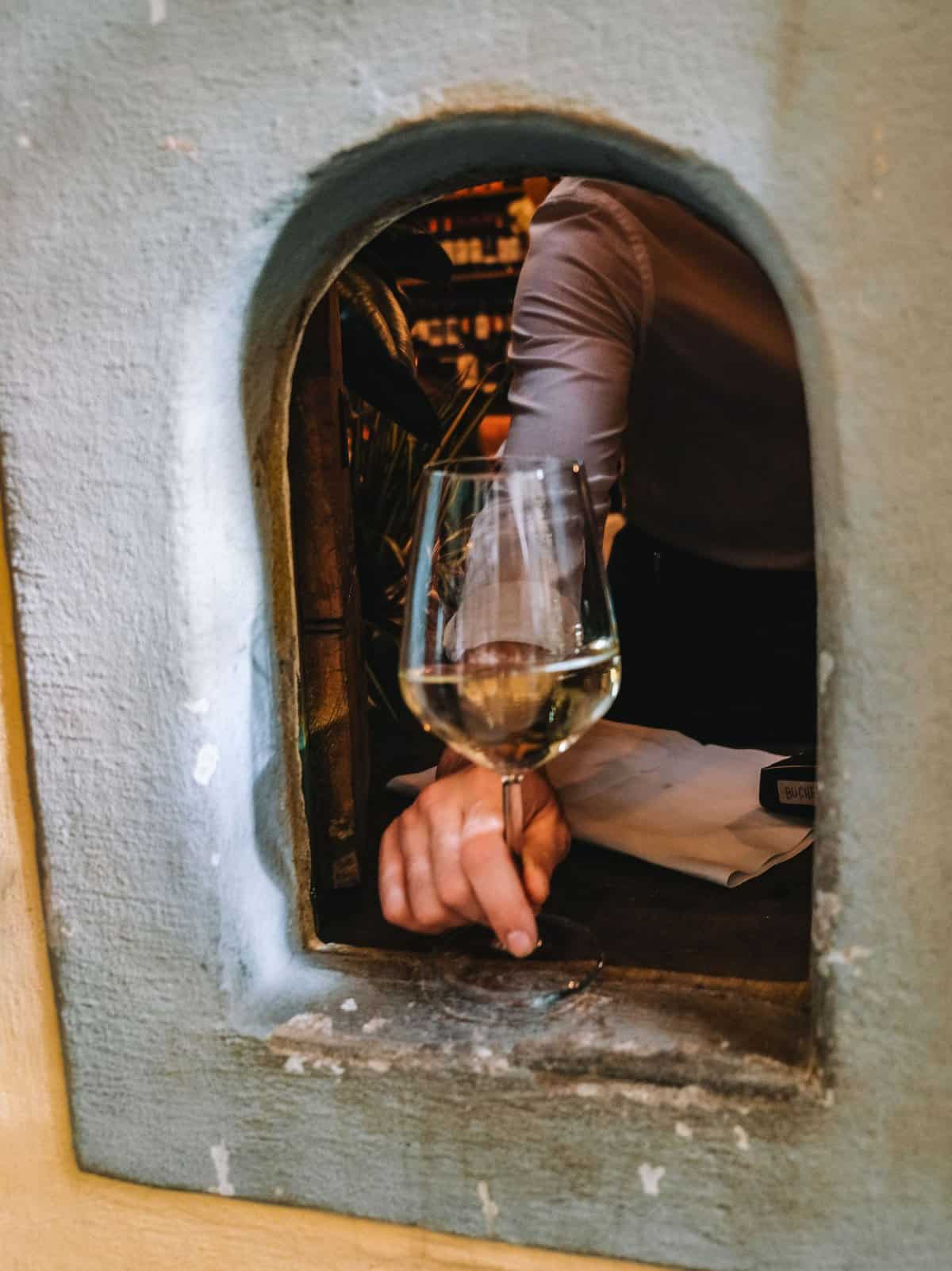 Receiving a glass of vino bianco through a wine window in Florence. 