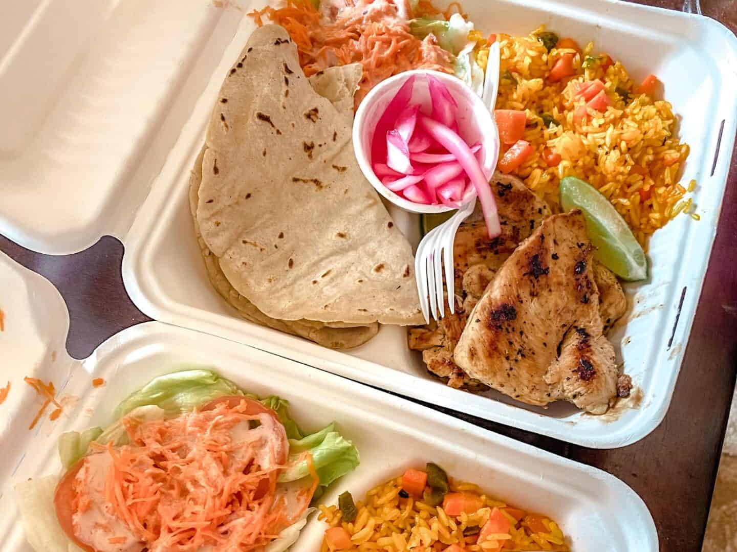 Two heaping take-out containers filled with jerk chicken, tortillas, rice and beans