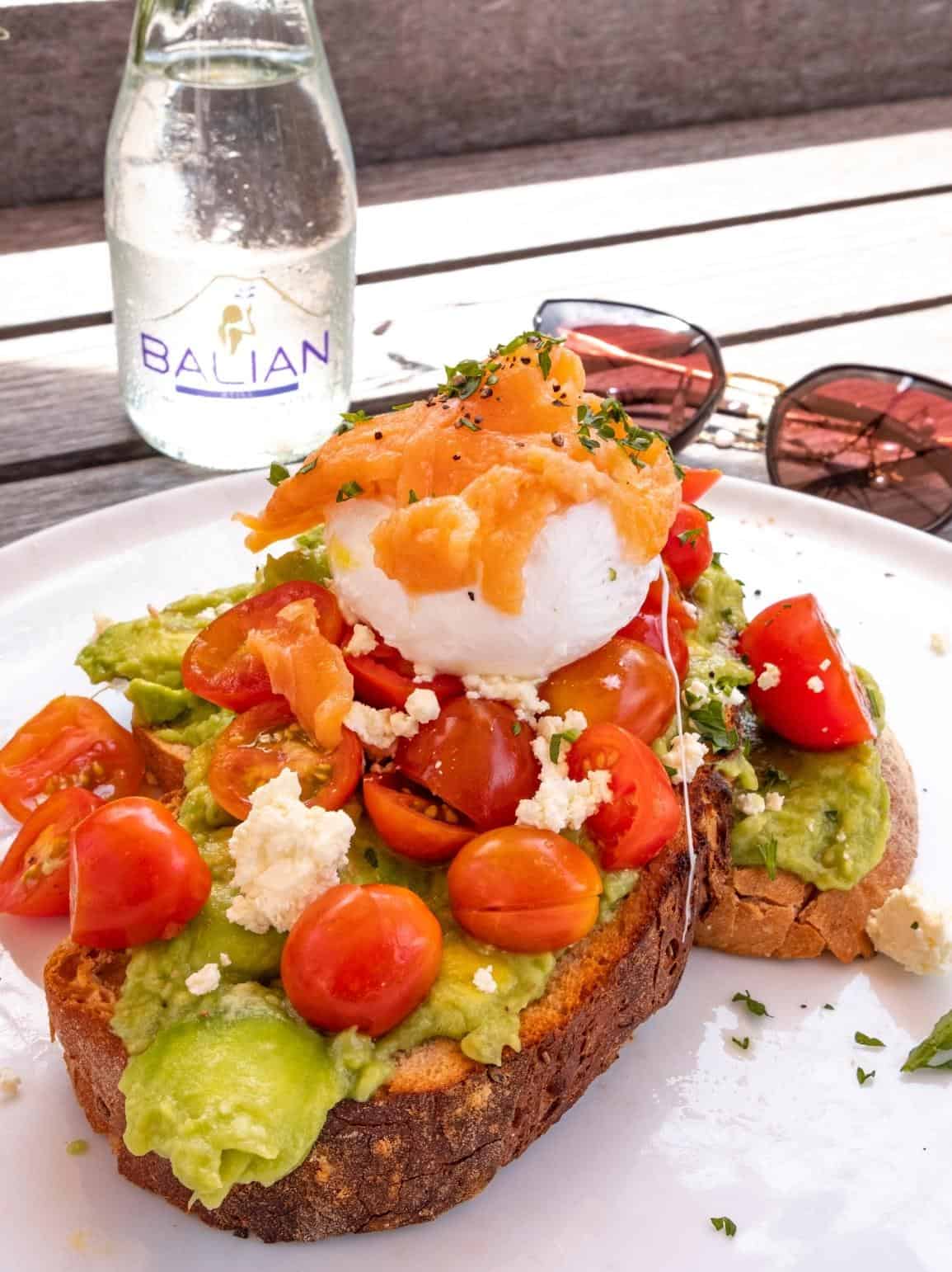 Avocado toast piled high with cherry tomatoes, feta, smoked salmon and a poached egg