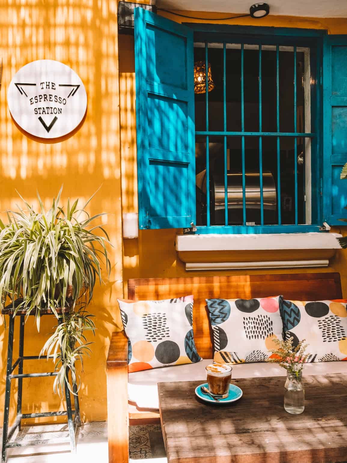 The outdoor patio of The Espresso Station coffee shop in Hoi An—the walls are bright yellow and the shutters are bright blue. 