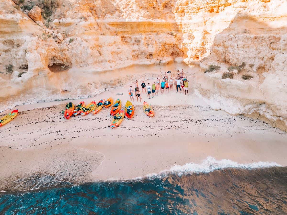 A drone shot of our sea kayaking tour group waving on the beach with our orange and red kayaks in front of us. 