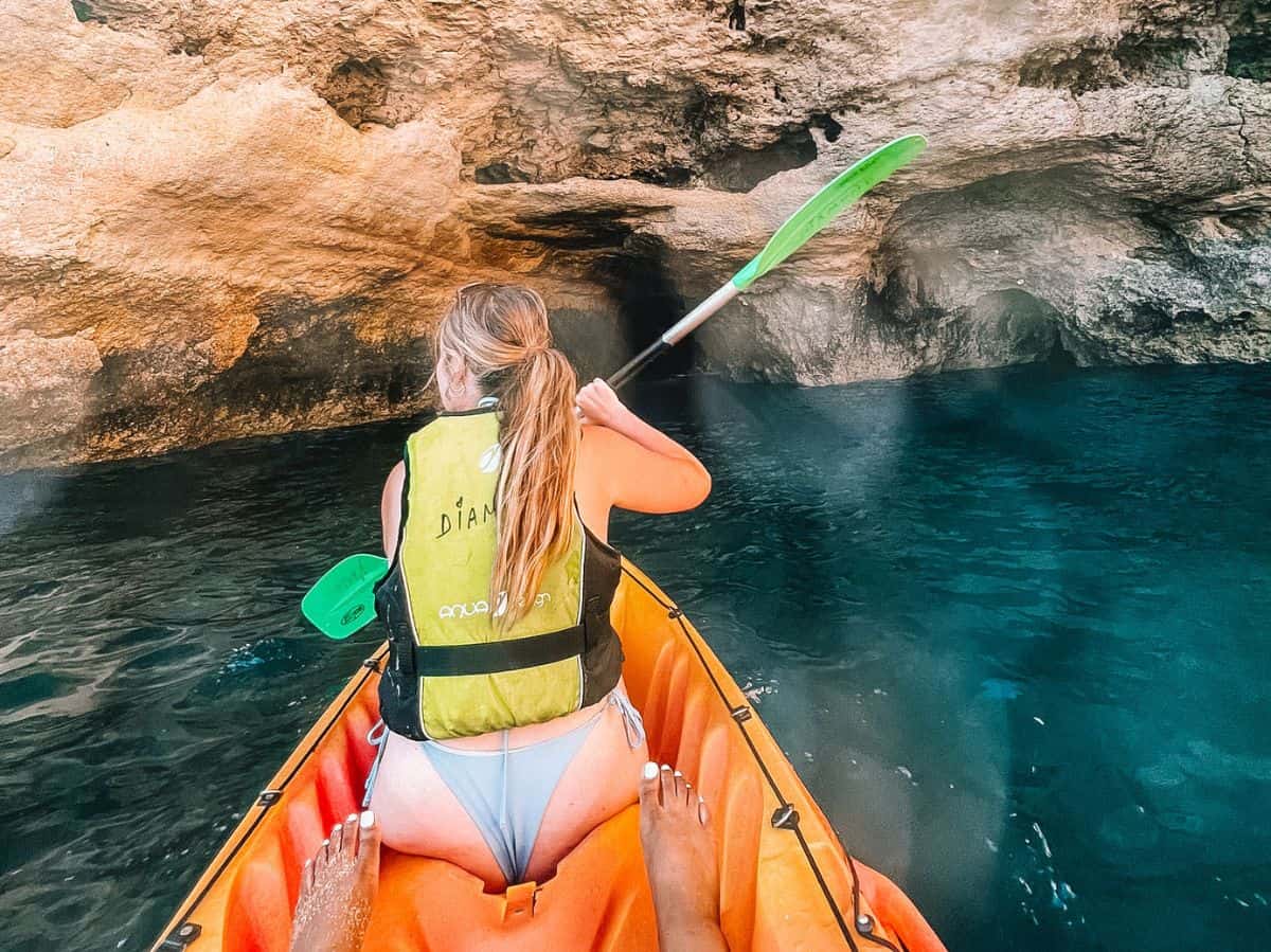 My friend in the front of an orange, two-person kayak, kayaking her way through the caves of Lagos.