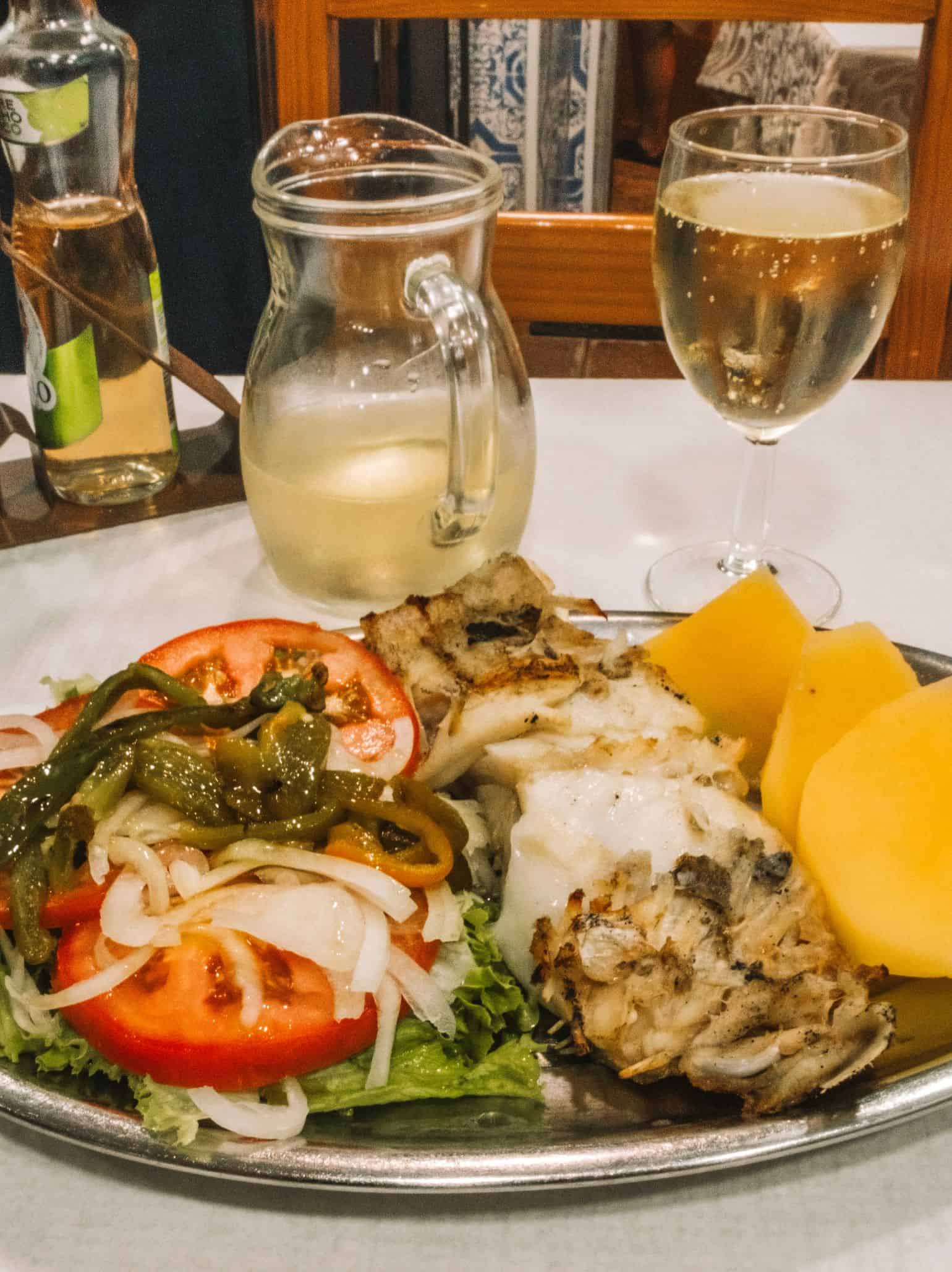 Oven-baked cod with boiled potatoes, a side salad, and a carafe of vinho verde from O Caldo Verde in Lisbon.