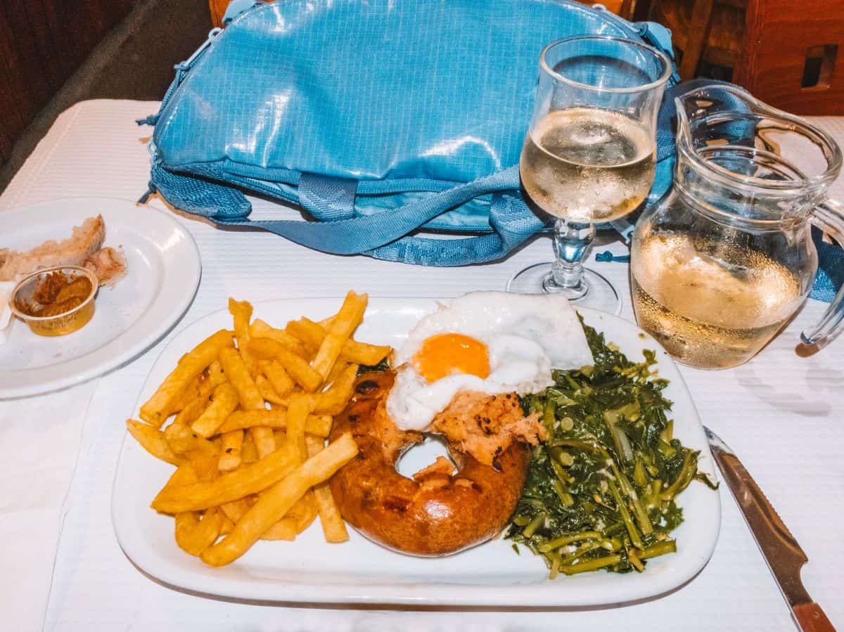 A plate of Alheira de Mirandela with french fries, salad, and a fried egg on top from Casa dos Passarinhos in Lisbon. 