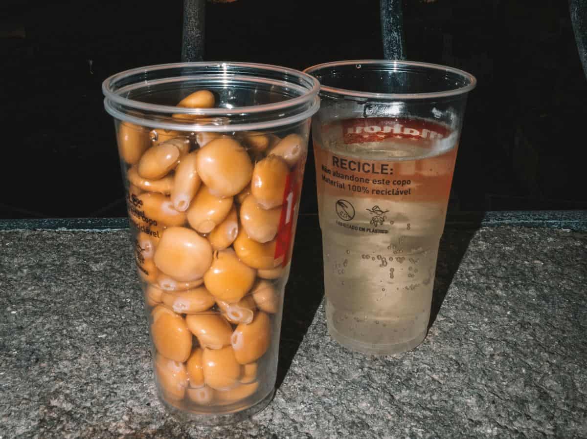Two plastic cups: one filled with vinho verde and one filled with lupini beans in Porto. 