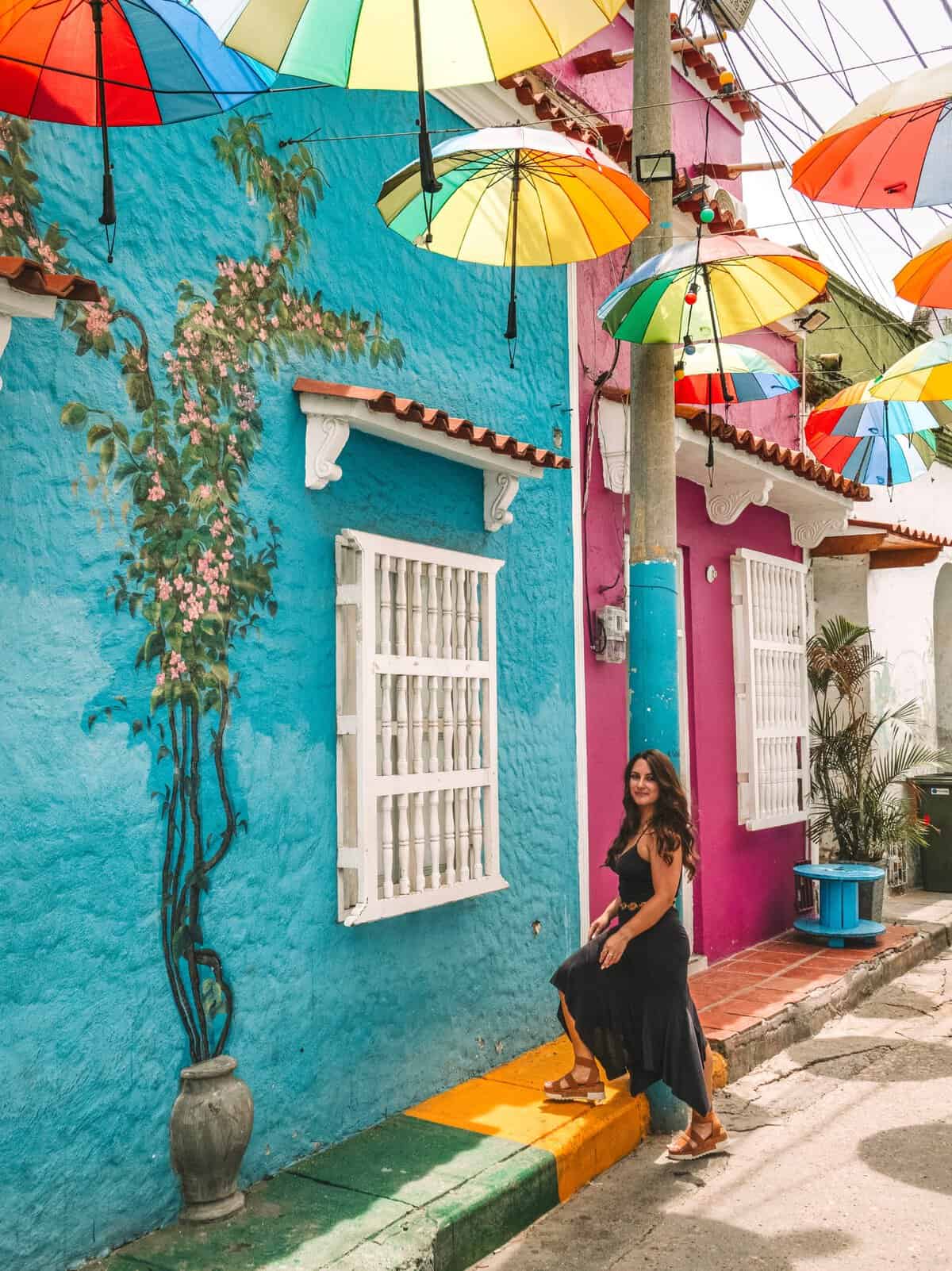 Me next to a colorful blue and pink wall on a street covered with umbrellas in Getsemani.